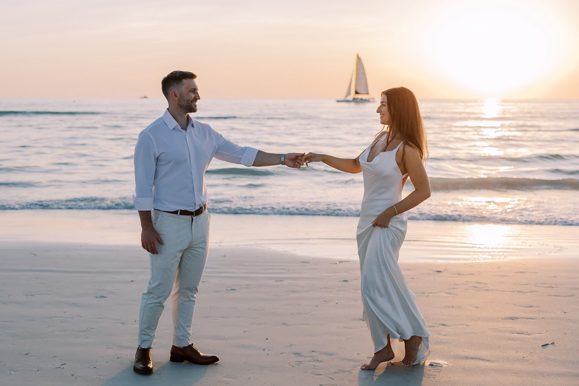 Groom Twirling Bride on the Beach at Sunset with Sailboat on the Gulf | Clearwater Beach Venue Sandpearl Resort
