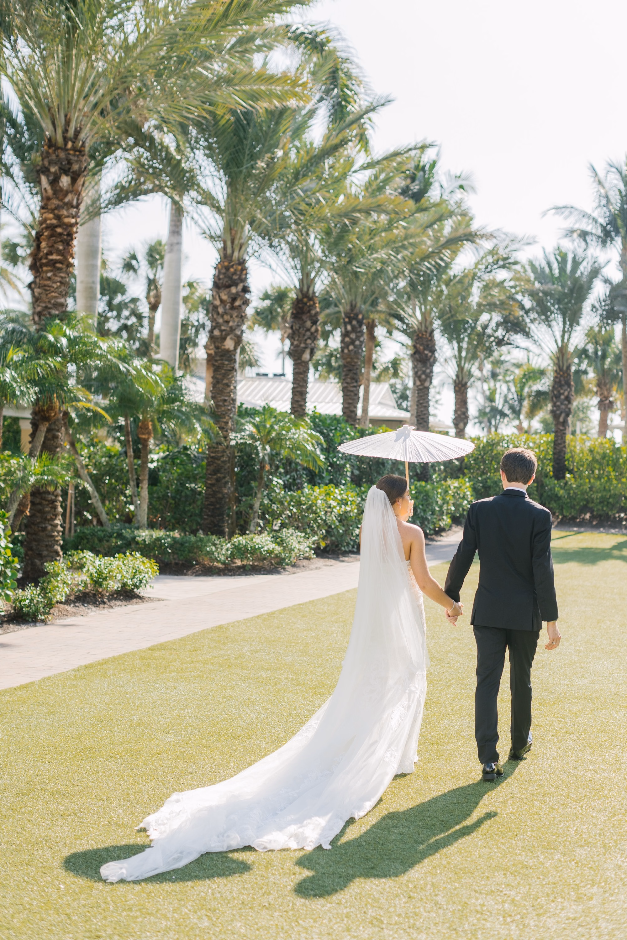24Luxurious Romantic Garden Ballroom Wedding Inspiration - Luxurious Garden-Inspired Naples Wedding | Hyatt Regency Coconut Point Bride and Groom Walking Wedding Portrait with Ivory Parasol | Cathedral Length Veil and Lace Mermaid Gown Inspiration | Tropical Resort Lawn Wedding Portrait Ideas | Bonita Springs Venue Hyatt Regency Coconut Point