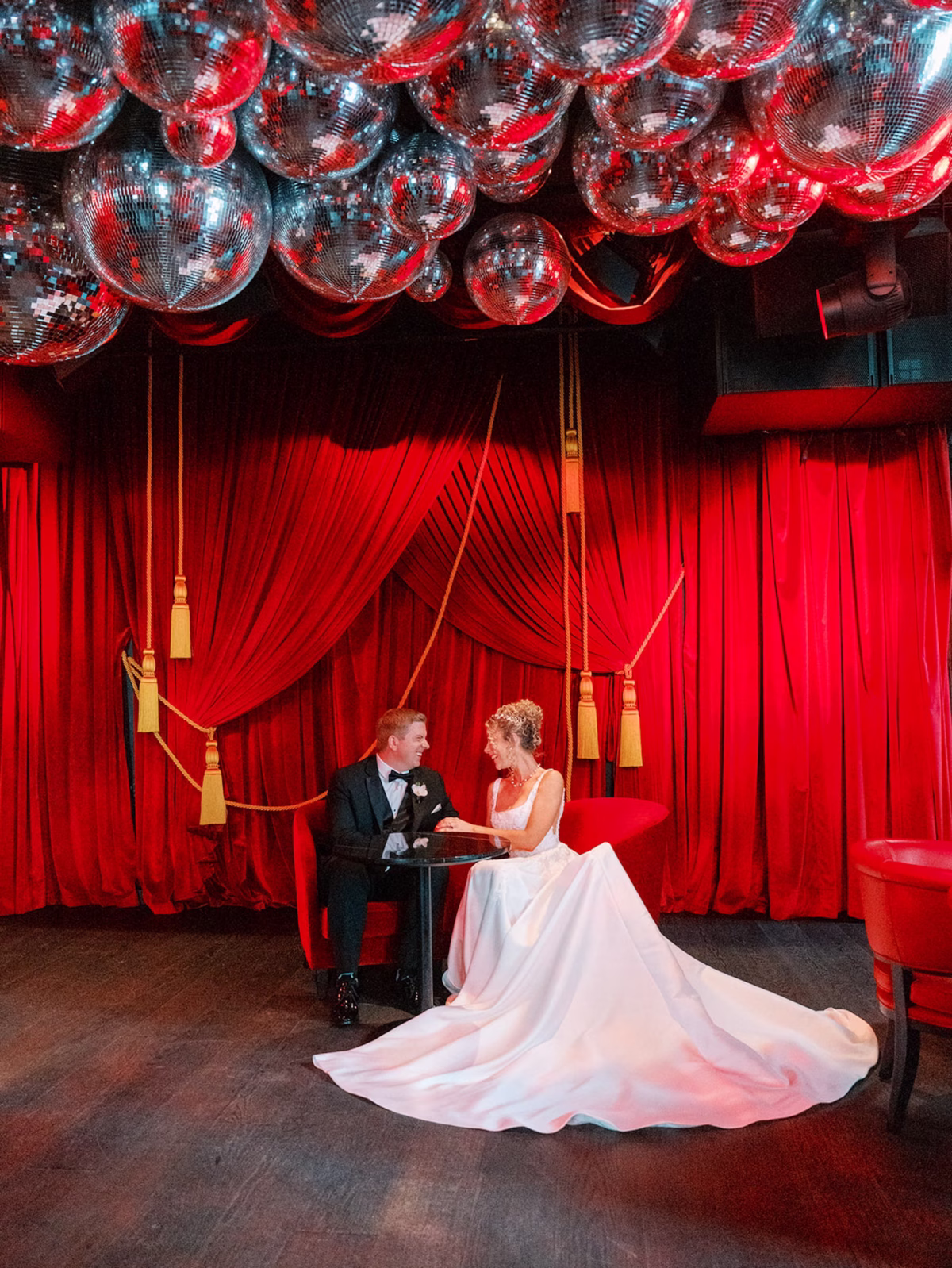 Bride and Groom Seated Under Disco Ball Ceiling in Red Velvet Curtain Lounge with Gold Tassels Wedding Portrait | Tampa Bay Photography Eddy Almaguer Photography | Event Venue The Edition