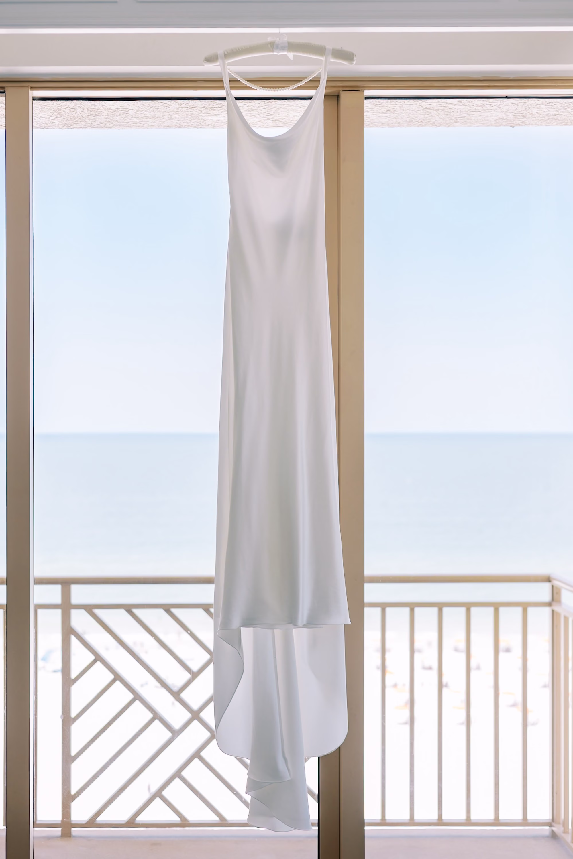 White Satin Slip Wedding Alexandra Grecco Dress Hanging on Balcony Overlooking the Gulf Beach