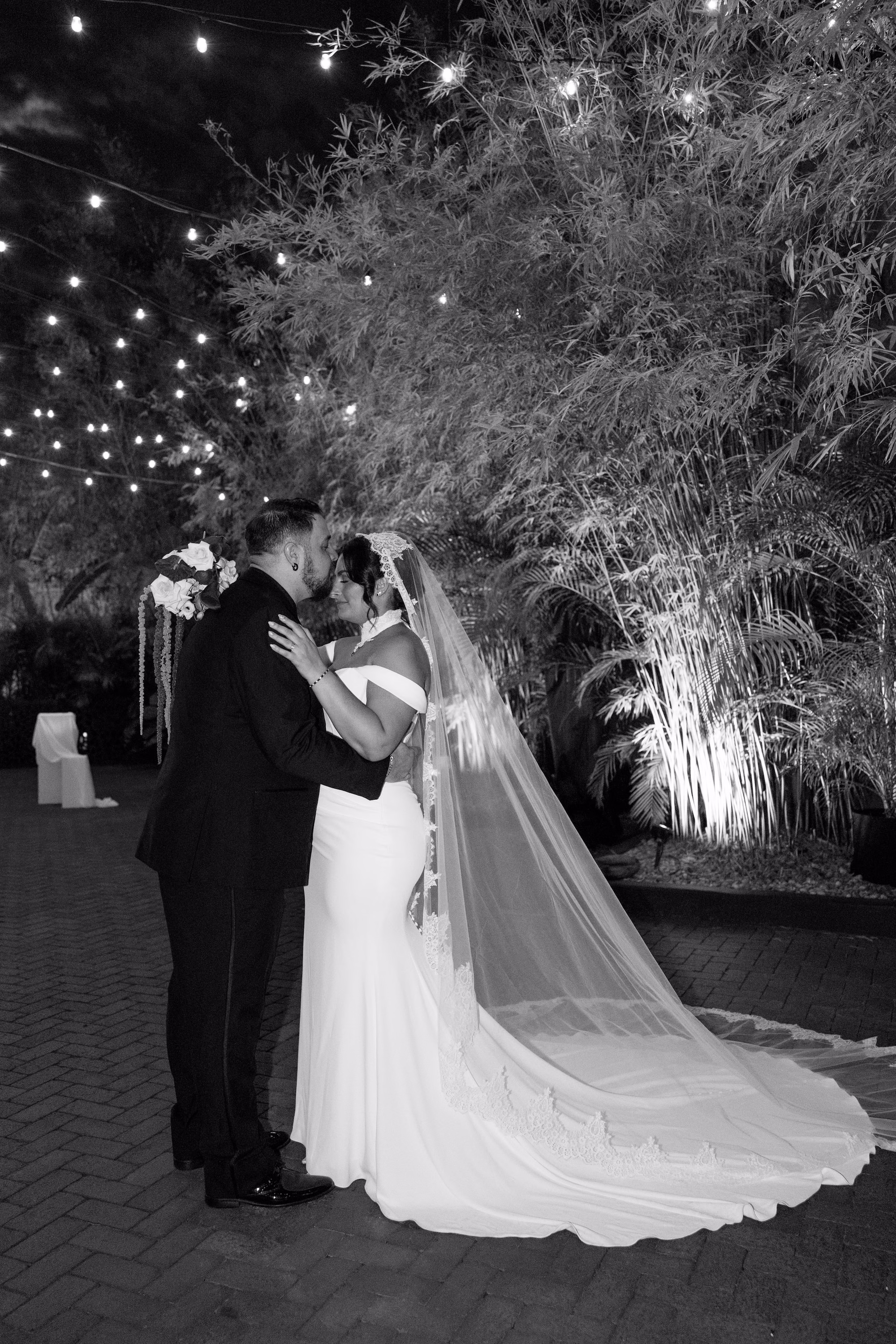 32Burgundy Vintage Romance Wedding Ideas St Pete Venue NOVA 535 - Vintage Romance Pink and Burgundy Downtown St. Pete Wedding | NOVA 535 Black and White Night Portrait of Bride and Groom Kissing Under String Lights in Bamboo Courtyard | St. Pete Venue NOVA 535