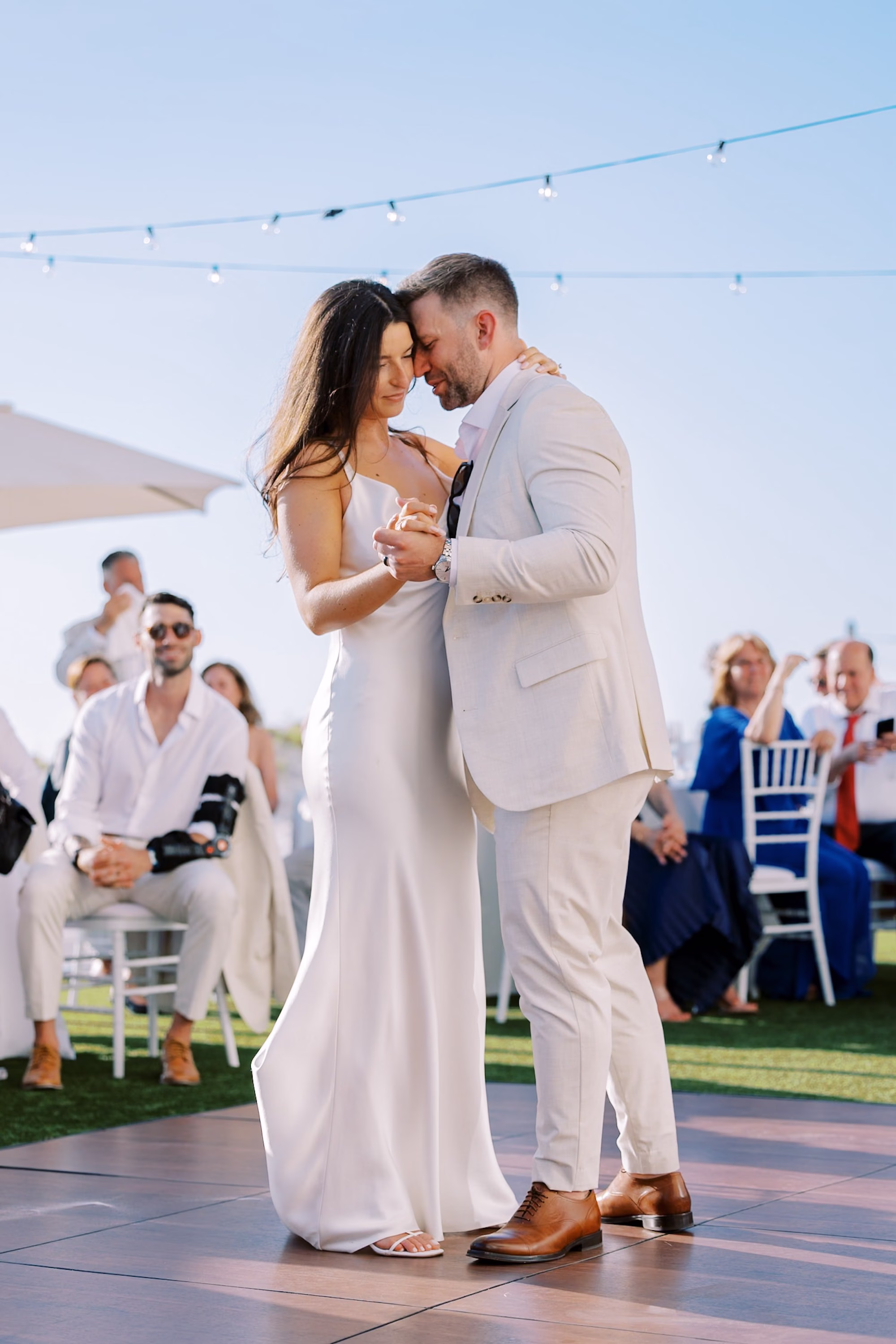 Bride and Groom First Dance on Outdoor Dance Floor Under String Lights at Beachfront Lawn Reception