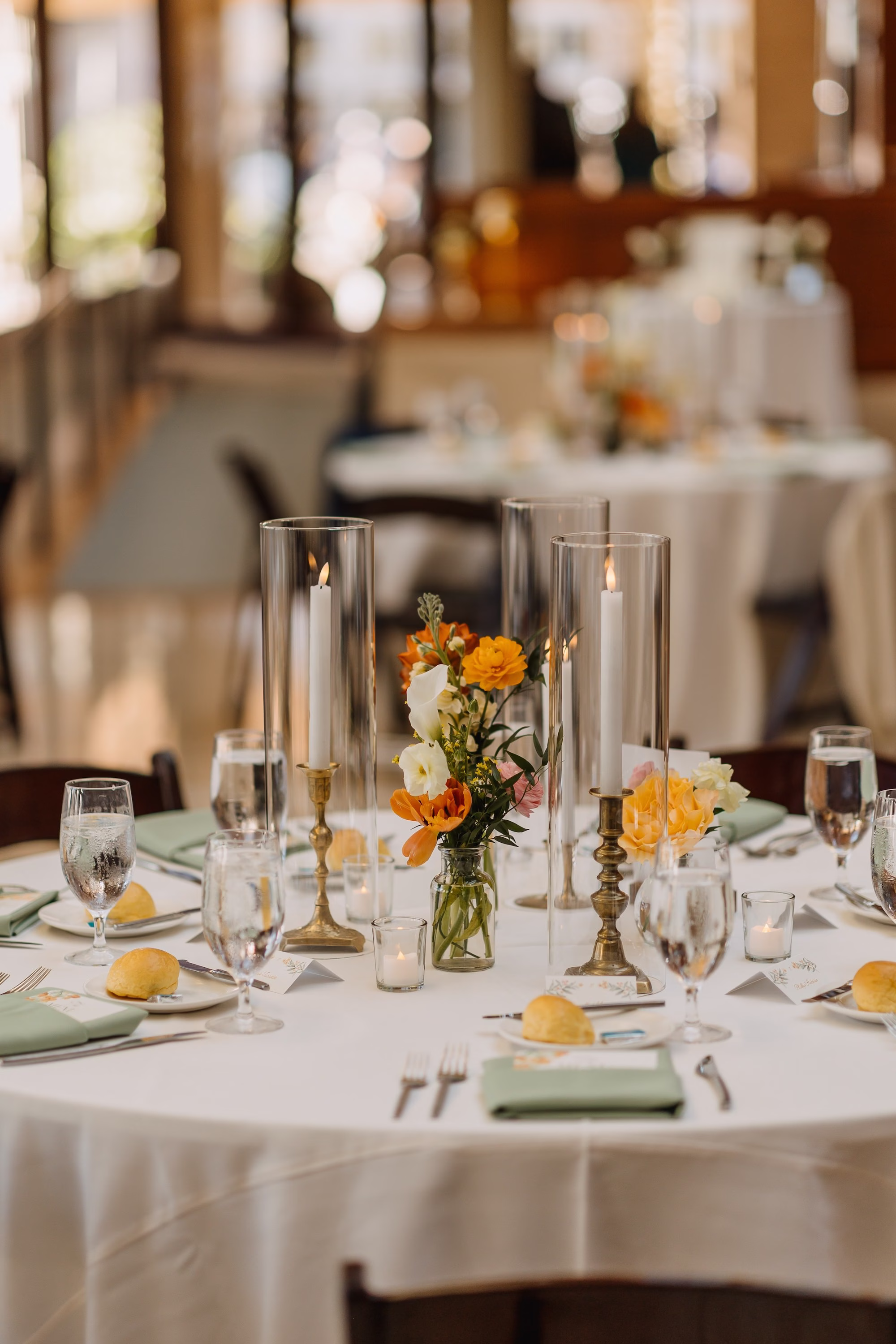 Wedding Reception Table with Tall Glass Candle Holders, Orange Floral Bud Vase Centerpiece and Sage Green Napkins Decor Ideas | St. Pete Planner Coastal Coordinating | Florist Monarch Events and Design