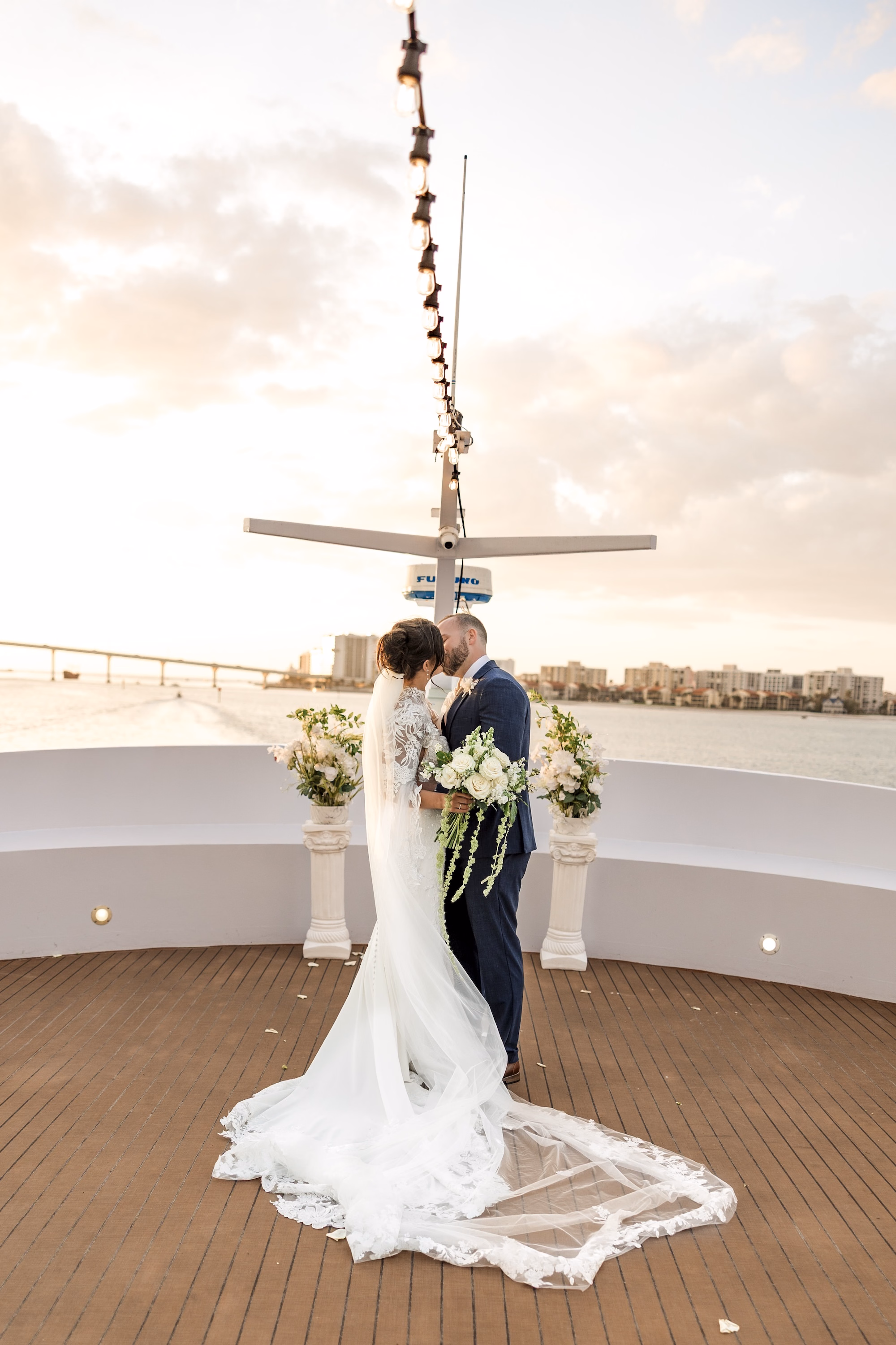 Bride and Groom Kissing on Yacht Top Deck at Sunset Wedding Portrait | White Rose Bouquet with Cascading Greenery Inspiration | Floral Lace Cathedral Length Veil Ideas | Clearwater Wedding Venue Yacht StarShip