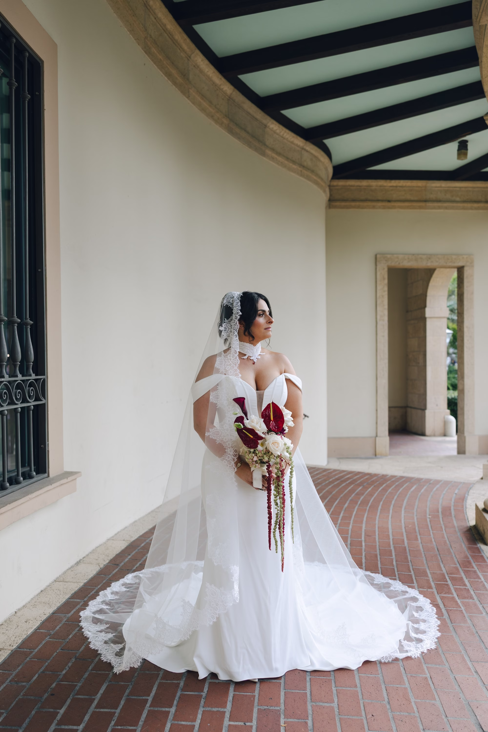3Burgundy Vintage Romance Wedding Ideas - Vintage Romance Pink and Burgundy Downtown St. Pete Wedding | NOVA 535 Bride in Off-the-Shoulder White Fit and Flare Wedding Dress with Lace Veil Holding Burgundy and White Bouquet Under Covered Arched Walkway