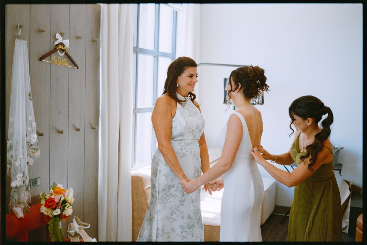 Bride Getting Ready with Mother and Bridesmaid in Olive Green Dress Buttoning White Sheath Wedding Gown