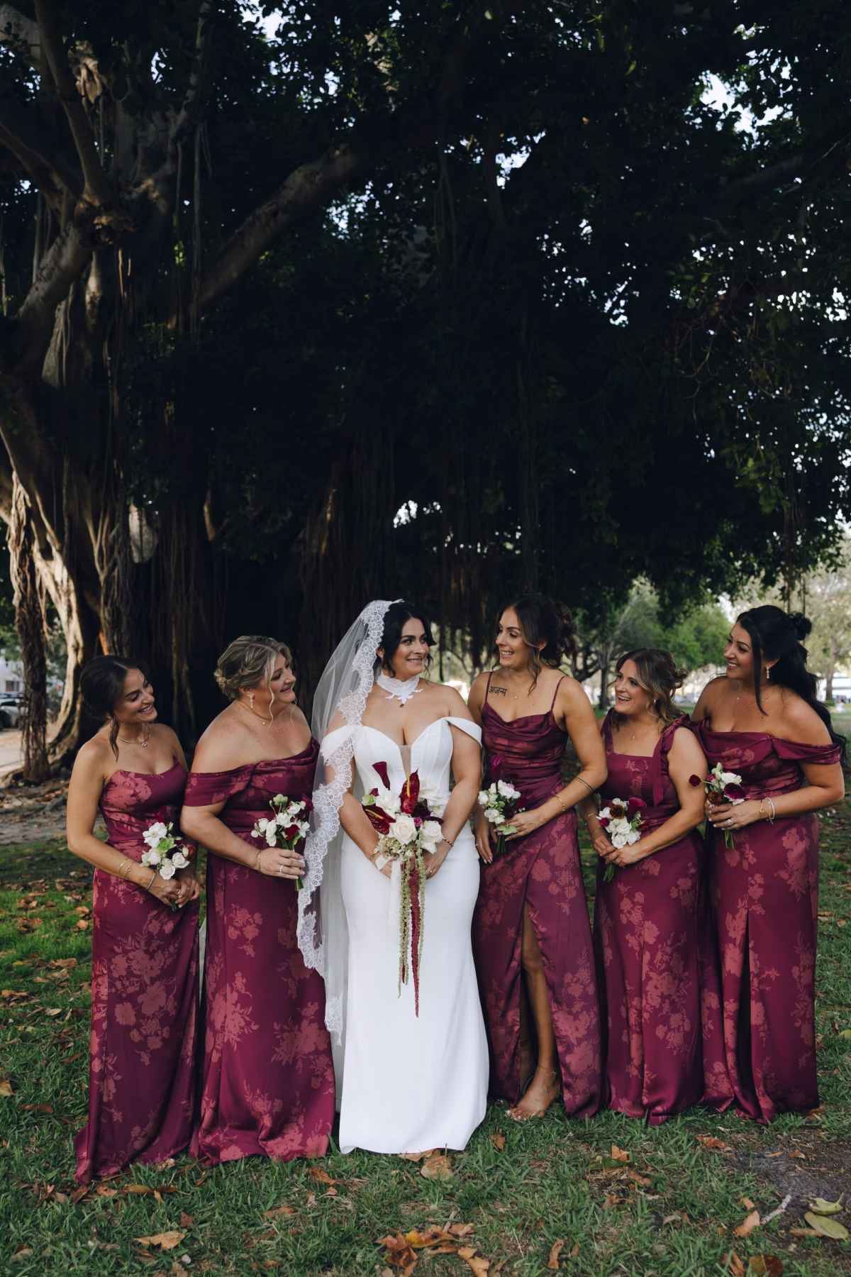 7Burgundy Vintage Romance Wedding Ideas - Vintage Romance Pink and Burgundy Downtown St. Pete Wedding | NOVA 535 Bride with Bridesmaids in Mismatched Burgundy Satin Dresses Holding White and Burgundy Bouquets Under Banyan Tree