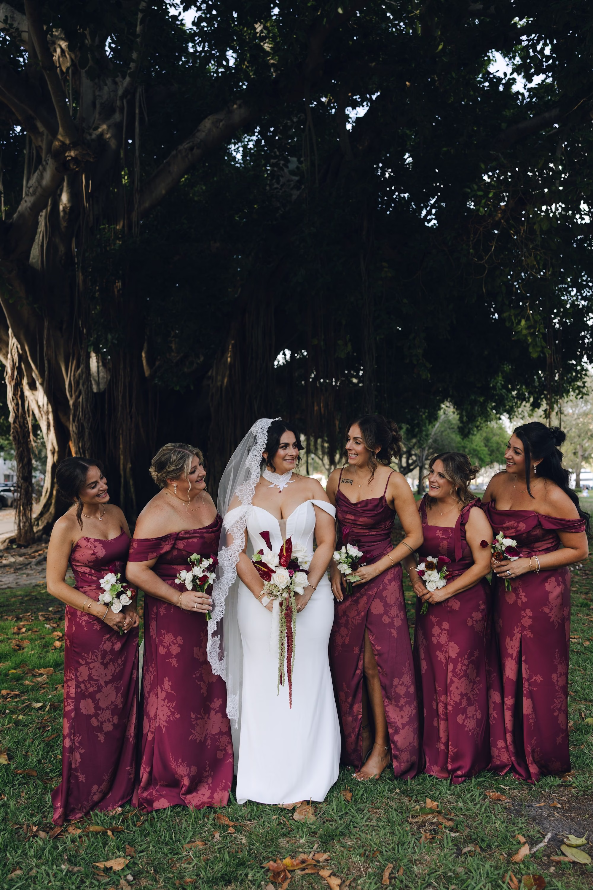 7Burgundy Vintage Romance Wedding Ideas - Vintage Romance Pink and Burgundy Downtown St. Pete Wedding | NOVA 535 Bride with Bridesmaids in Mismatched Burgundy Satin Dresses Holding White and Burgundy Bouquets Under Banyan Tree