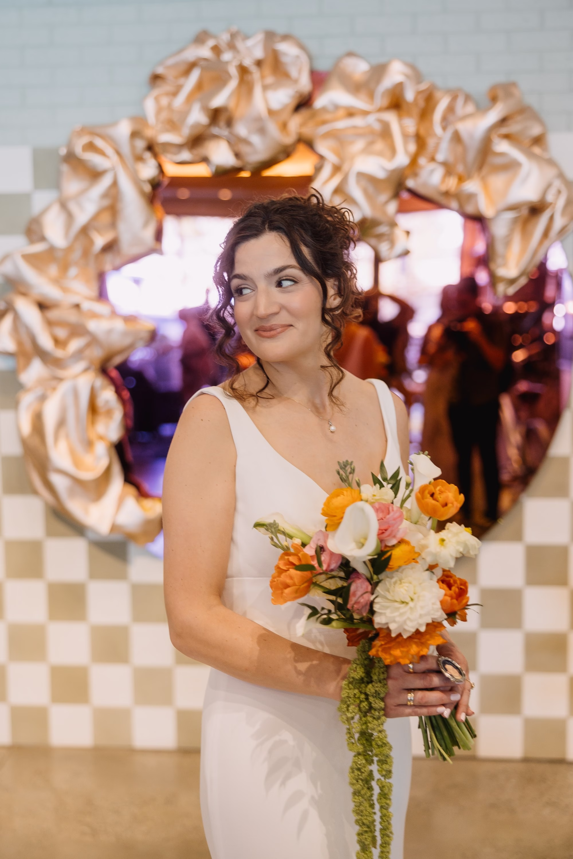 Bride in White Crepe V-Neck Sheath Wedding Dress with Orange, Peach and White Bouquet in Front of Gold Mirror and Checkered Wall | St. Pete Hair and Makeup Femme Akoi Beauty Studio | Florist Monarch Events and Design