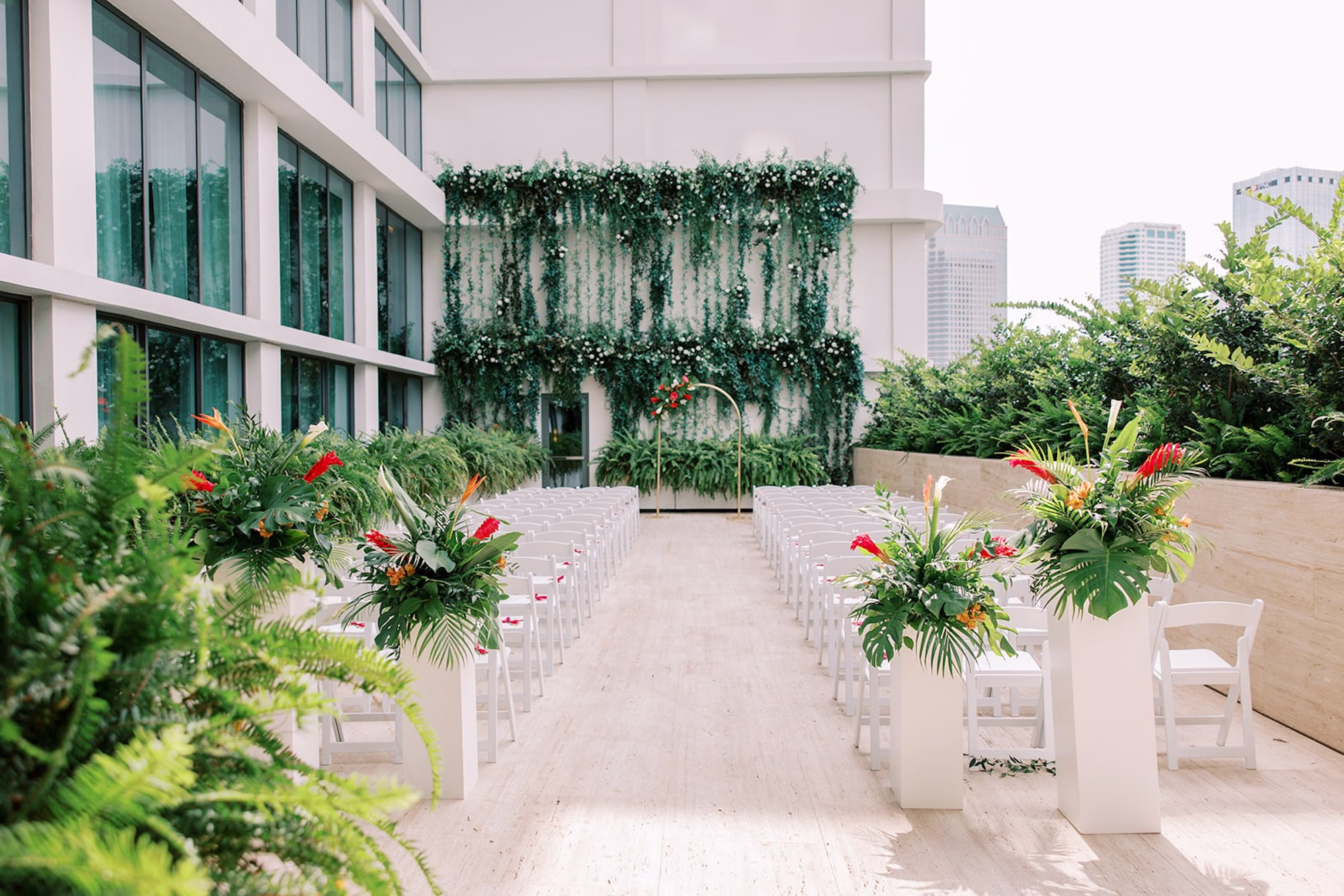 Rooftop Terrace Wedding Ceremony with Living Greenery Wall, White Folding Chairs and Tropical Floral Pedestal Arrangements Ideas | Tampa Planner Seashine Weddings & Events | Florist Monarch Events and Design | Venue The Edition
